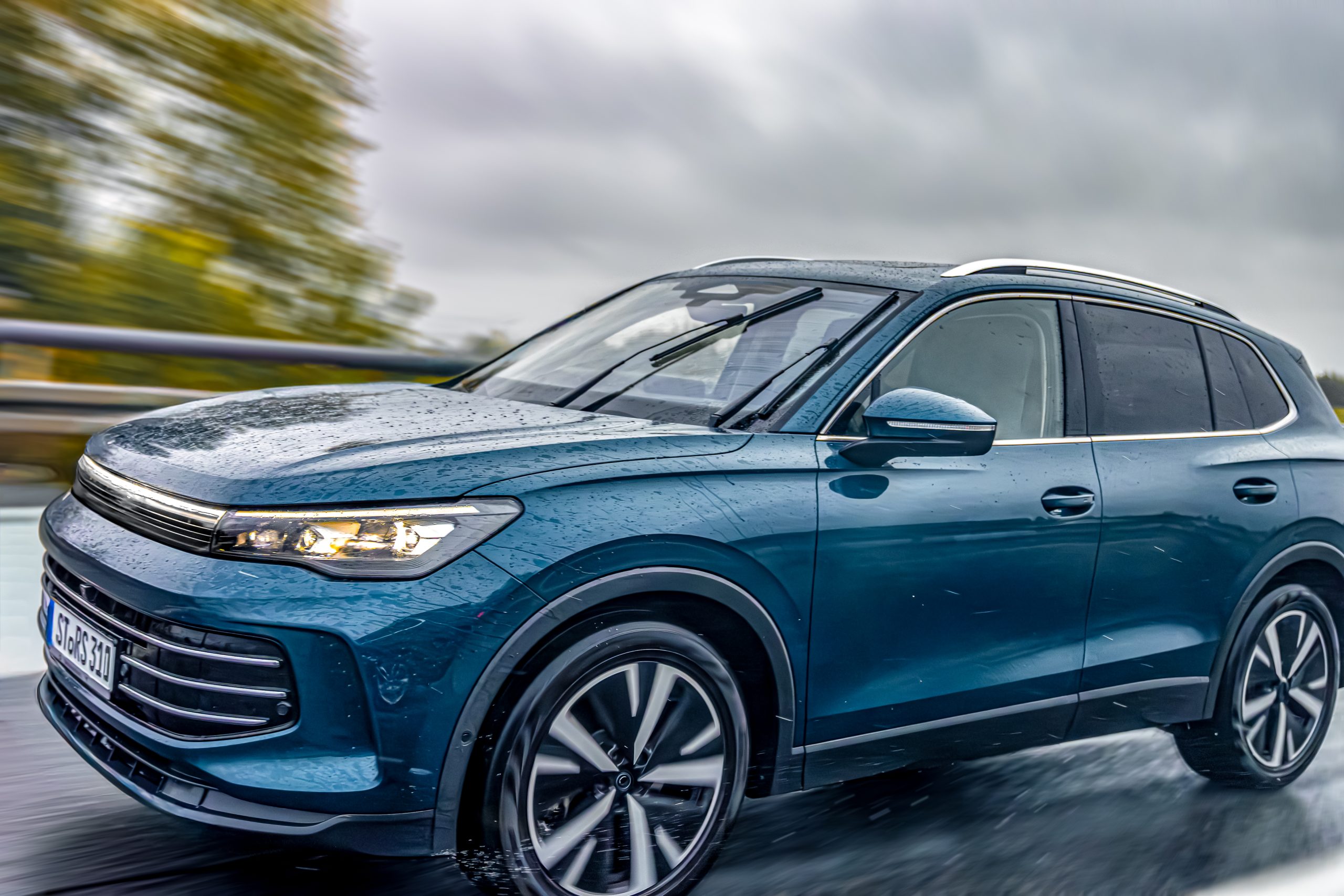 A modern blue SUV drives fast on a wet highway during rain. Raindrops, reflections, and motion blur create a dynamic and powerful automotive scene.