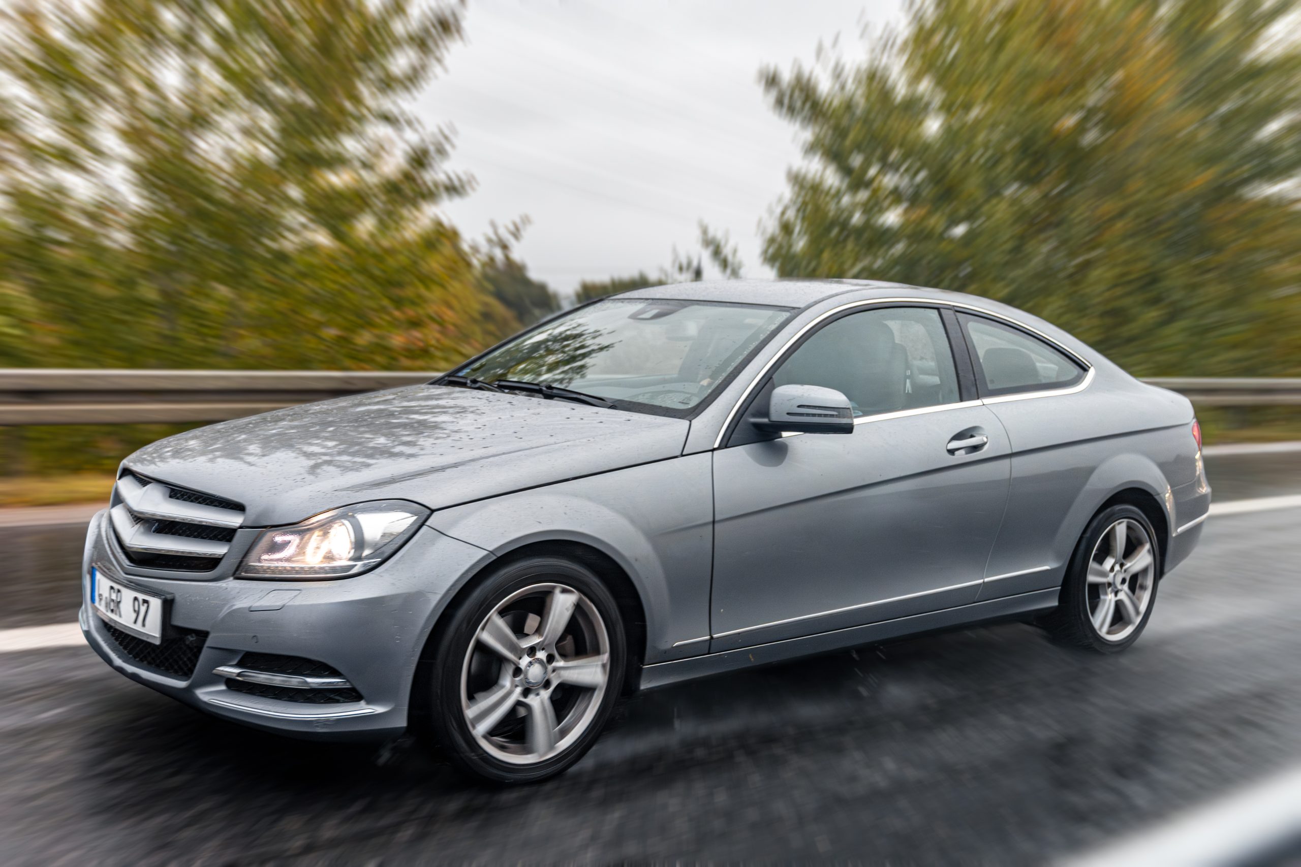 A modern gray coupe drives on a wet road after rain, water drops reflecting the light. The image captures motion, precision and the drive of modern travel.
